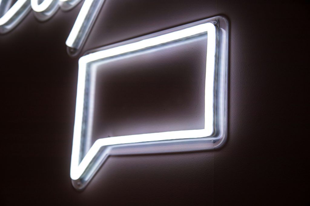 Eine weiße Neonröhre in Form einer Sprechblase auf einer schwarzen Wand